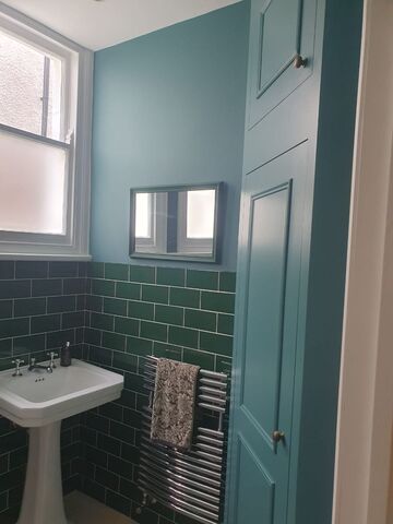 Teal painted bathroom walls and a tall panelled door with brass knobs beside dark green tiles