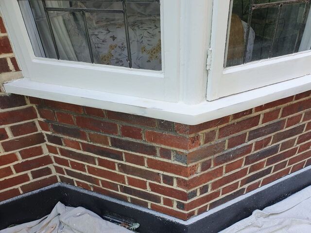 White painted bay window frames and sills above red brickwork