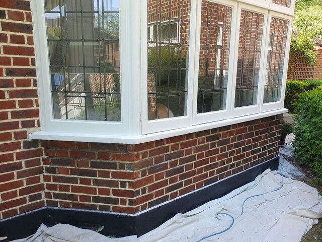 White painted bay window frames above red brickwork with dust sheets below