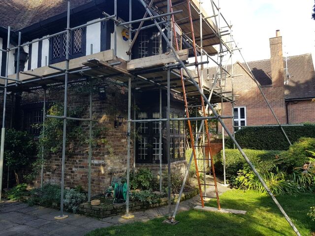 House under scaffold with a black and white timbered upper storey above brick, a ladder and planks