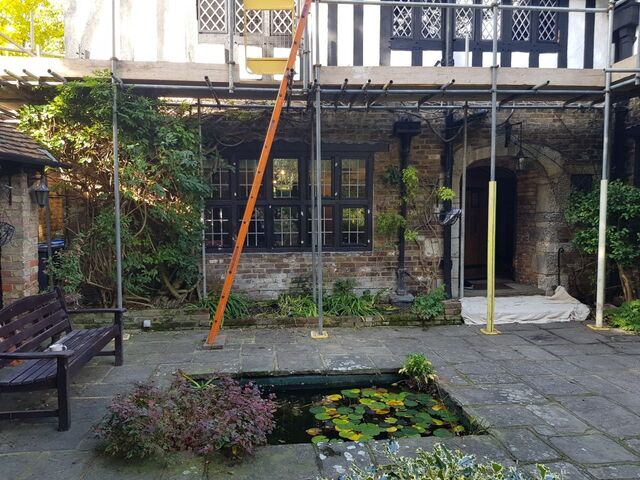 Courtyard with a lily pond, bench and flagstones before brick walls and a black framed window, scaffold up