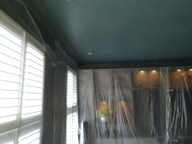 Dark green painted ceiling and cornice with the walls masked in plastic sheeting, mirror covered