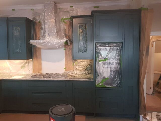 Dark green painted tall cupboard and wall units with worktops and oven masked in sheeting