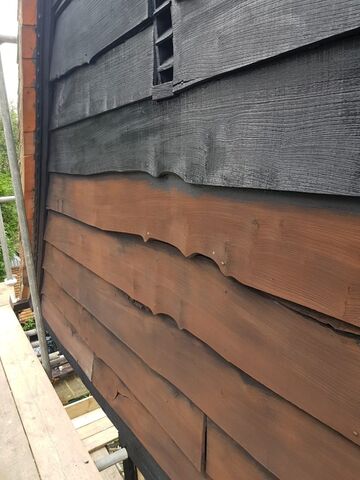 Gable weatherboarding close up, dark grey boards above brown timber below, scaffold plank at left