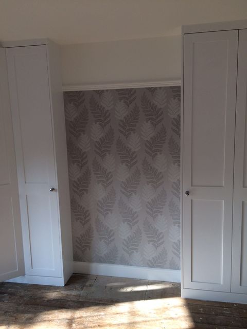 Fitted white cupboard against patterned wallpaper
