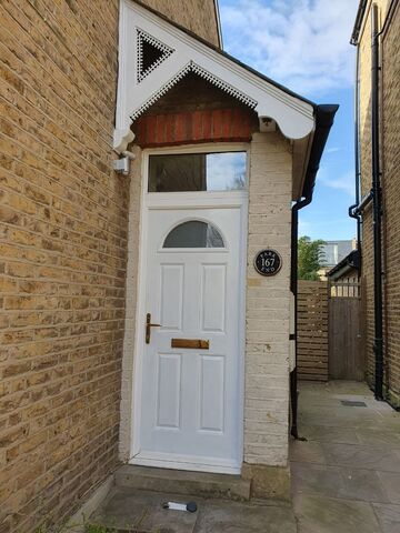 White painted front door with an arched panel below a decorative porch on a brick house
