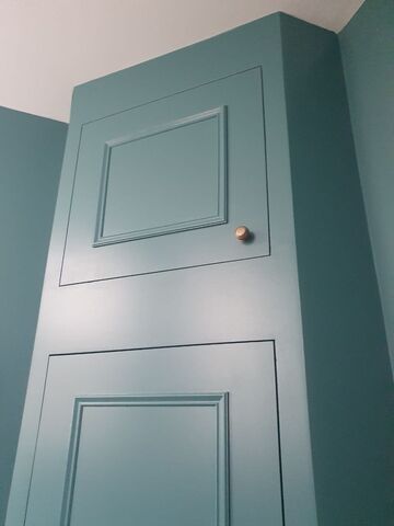 Tall teal painted panelled door with a brass knob against teal painted walls