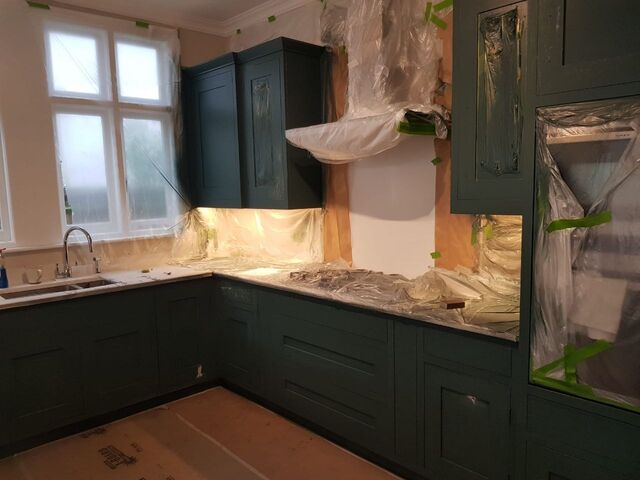 Kitchen with dark green painted units and a sink below a white-framed window