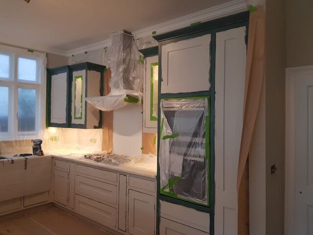 Kitchen unit frames painted dark green with the panel centres still white, walls and worktops masked