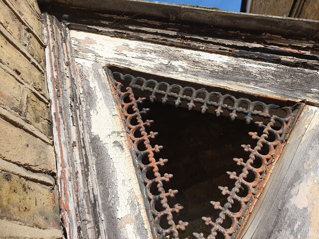 Stripped flaking timber fascia with a pierced metal trim around a dark opening