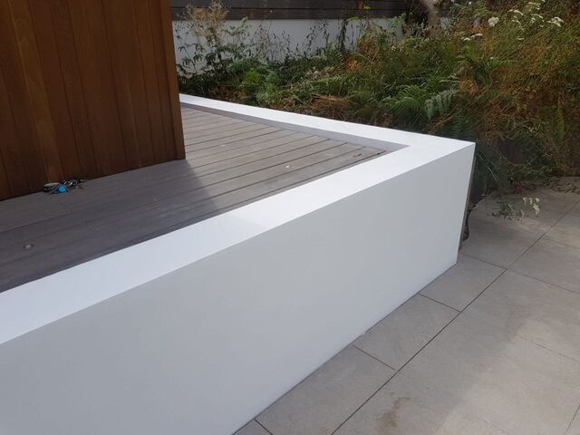 White rendered garden wall along grey paving slabs, with timber cladding and plants behind