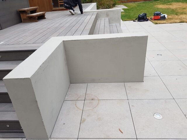 Rendered low wall beside grey composite decking steps, with grey paving and decking beyond