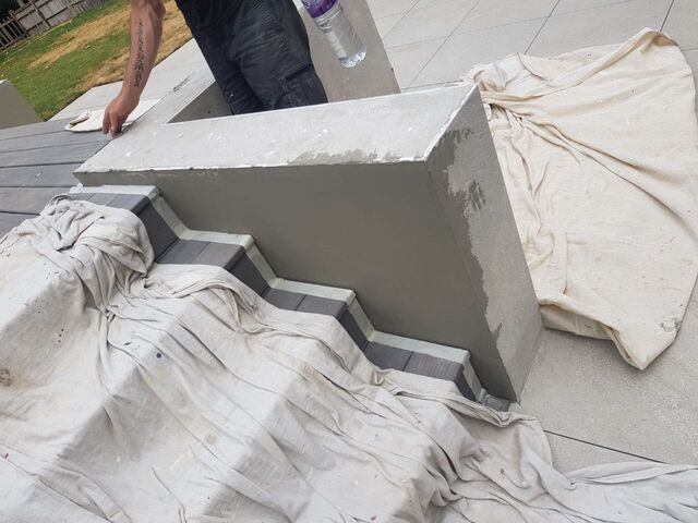 Grey rendered plinth with dust sheets over decking steps and paving, painter wiping it down