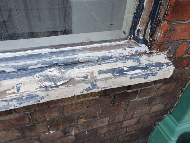 Window frame with stripped layers of old paint above brickwork