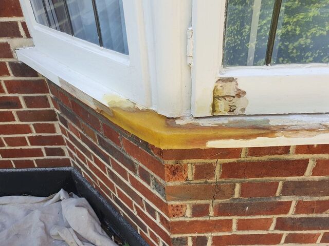 White painted sash window frames above brickwork with dust sheets on the ground below