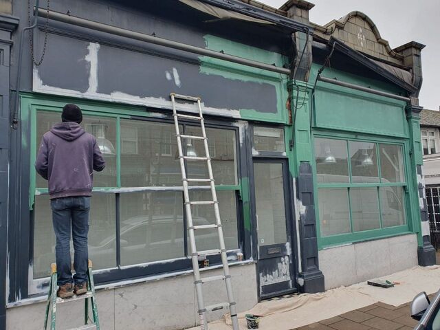 Decorator on a ladder painting the frame of a shopfront