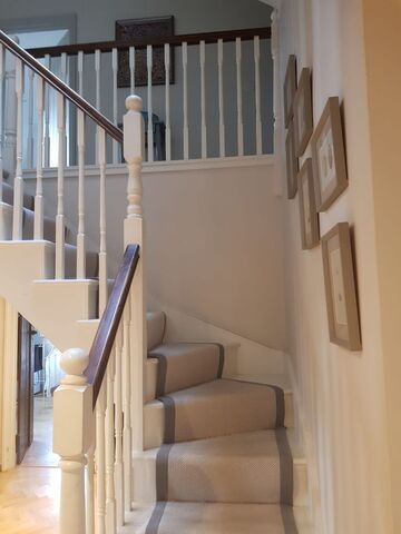 White painted spindles and newel post, dark timber handrail and a beige runner with a grey border