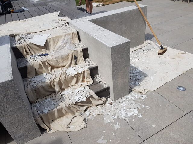 Scraped white paint flakes over canvas sheets on decking steps, with a scraper and broom on paving