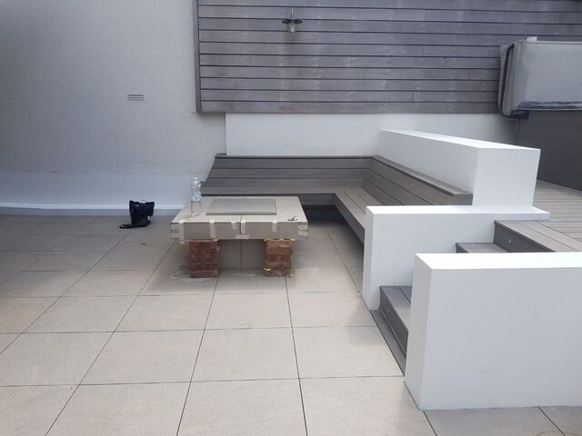 White painted rendered plinths and grey decking seating on a tiled terrace with timber slats above