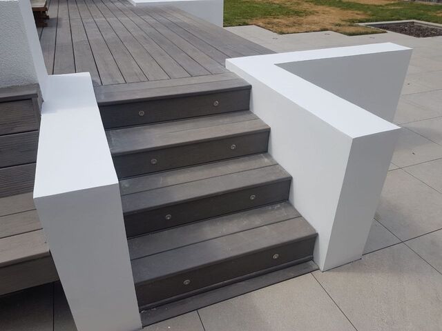 White painted rendered walls flanking grey composite decking steps, grey paving beyond