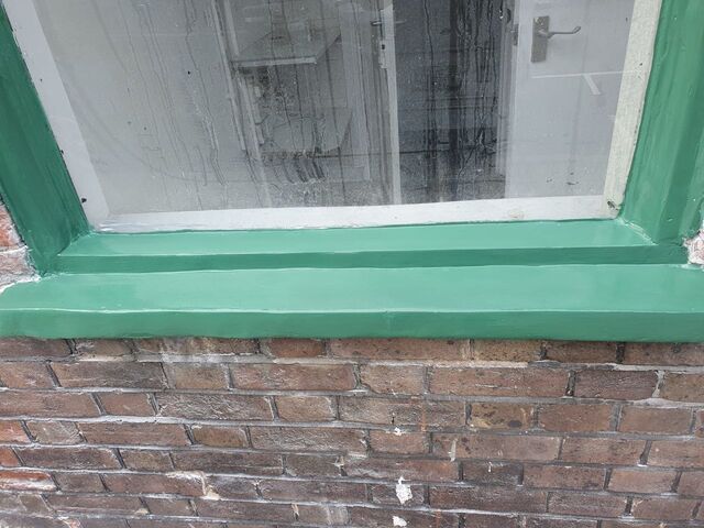 Green painted window frame and sill above red brickwork