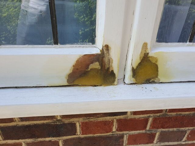 White painted window frame with patches stripped back to stained timber above red brick